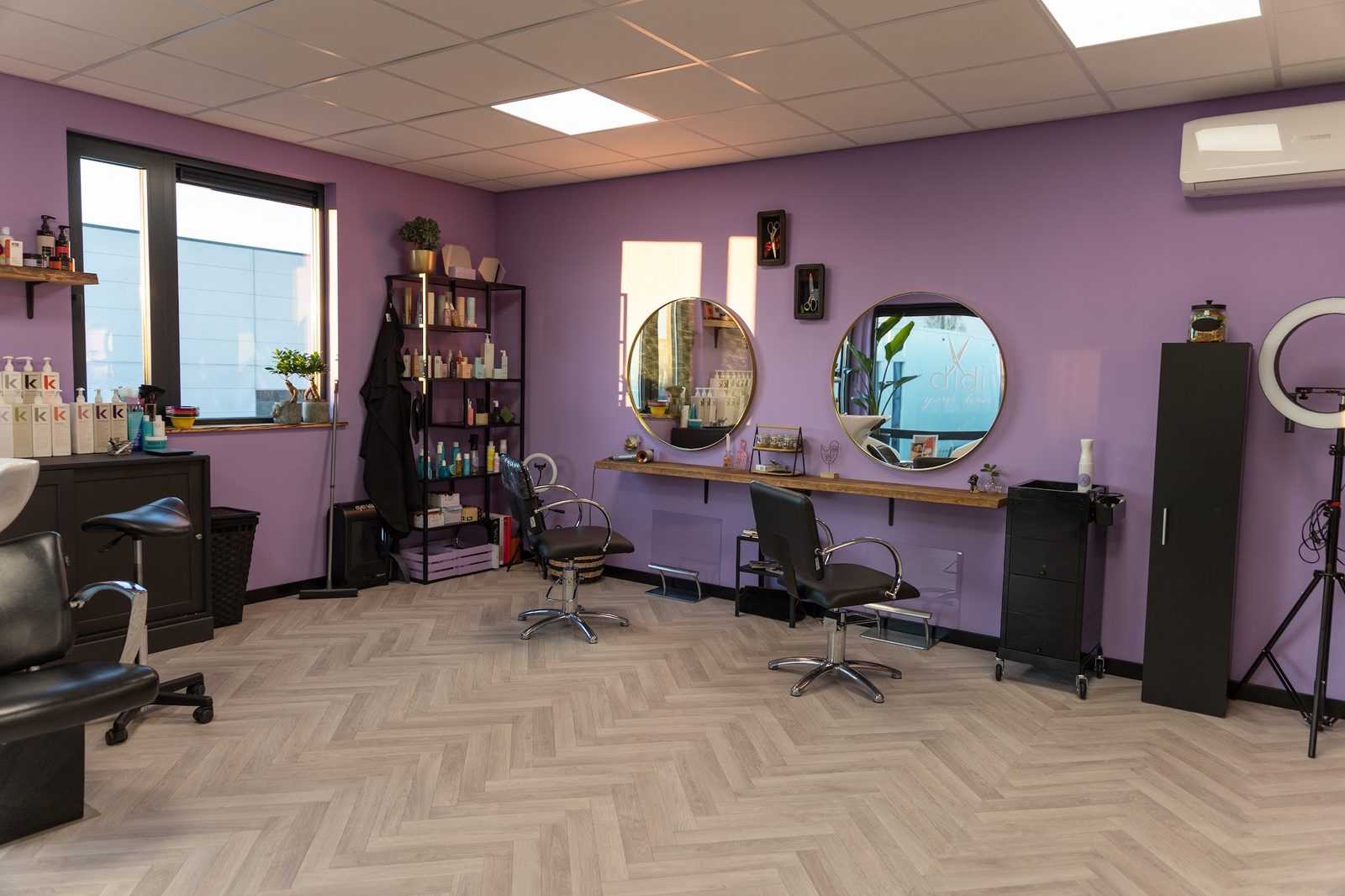 De salon met lila muren, twee ronde spiegels, de wasbak en een visgraatvloer